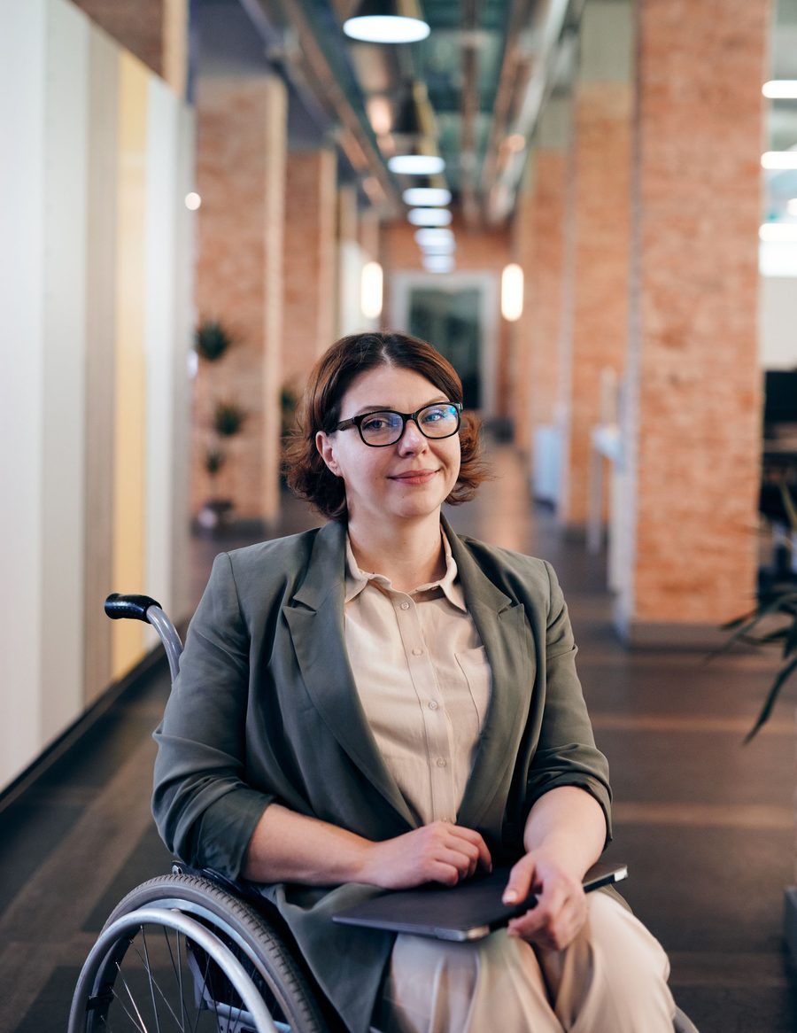 Une femme à lunettes sourit, assise dans un couloir de bureaux.