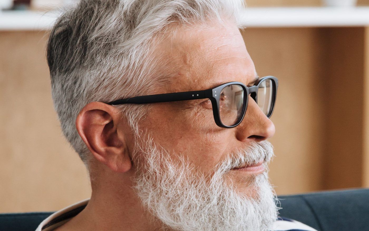 Un homme aux cheveux et à la barbe blancs, avec des lunettes, regarde au loin.